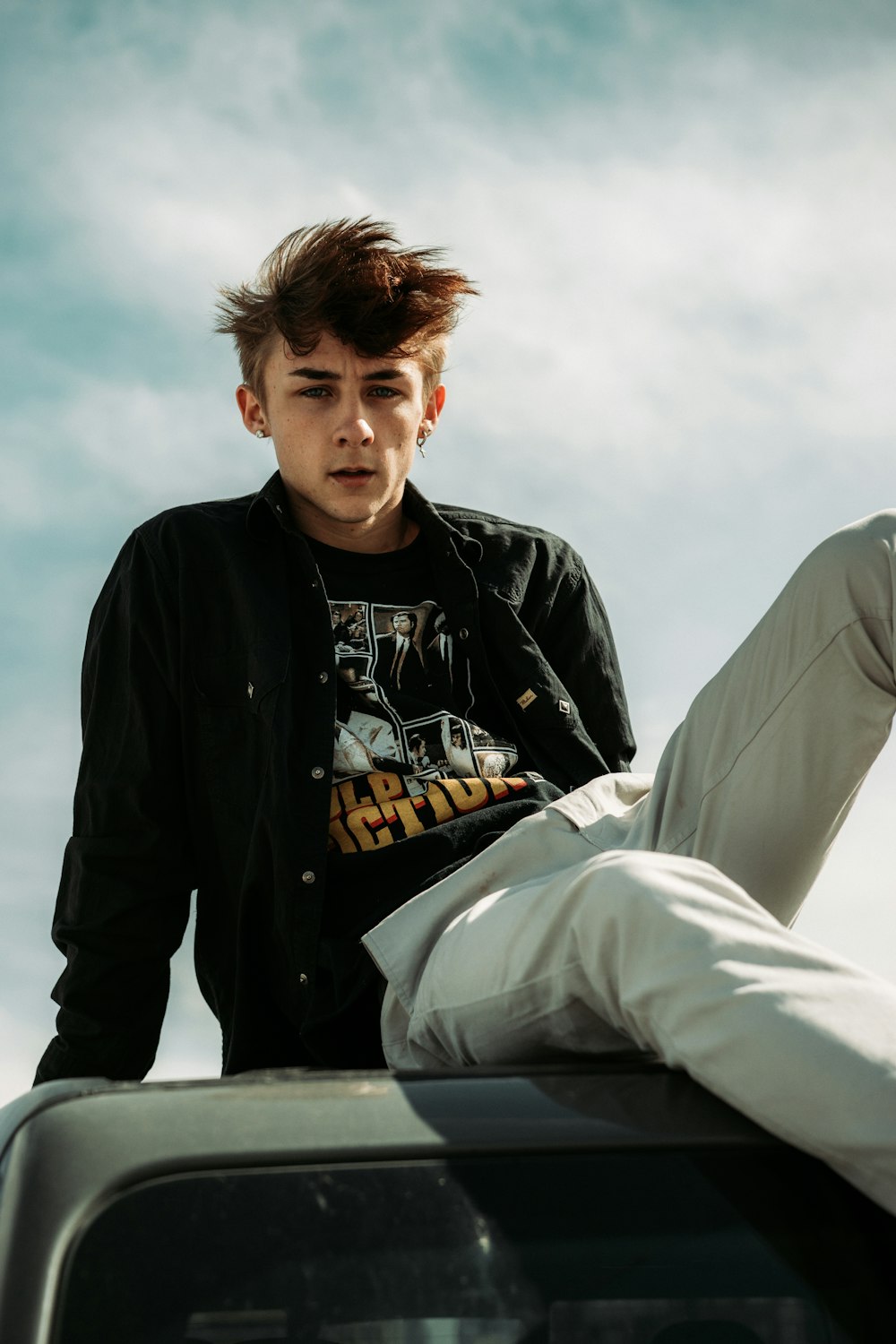 man in black jacket and white pants sitting on concrete wall