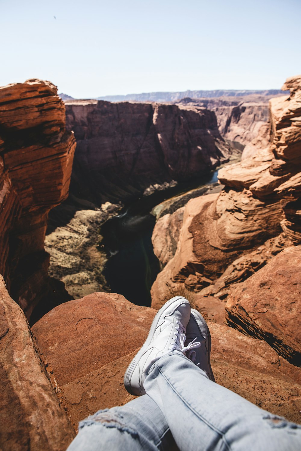 person in white sneakers sitting on brown rock formation during daytime