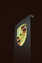 Stylish black and gold logo of Swiss Carpoint illuminated against a dark grey wall.
