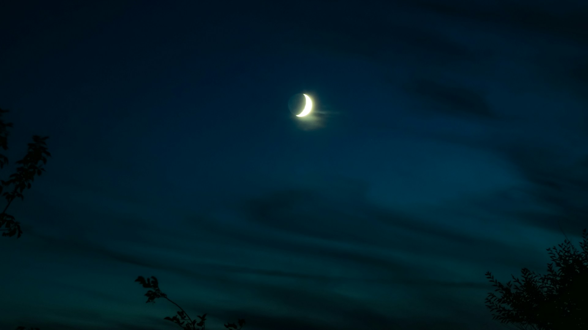 A close-up of a silver crescent moon pendant glowing softly against a dark, rainy window background.