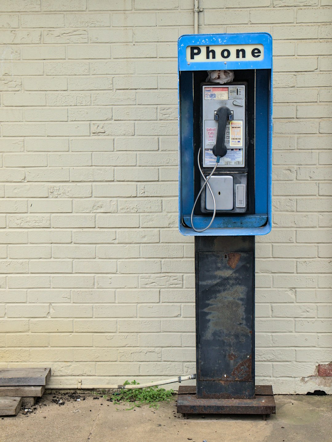 blue telephone booth mounted on white brick wall