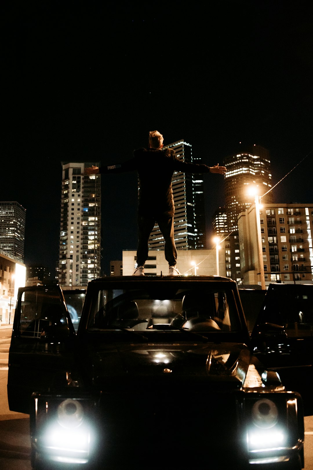 man in black t-shirt and black pants standing on black car during night time