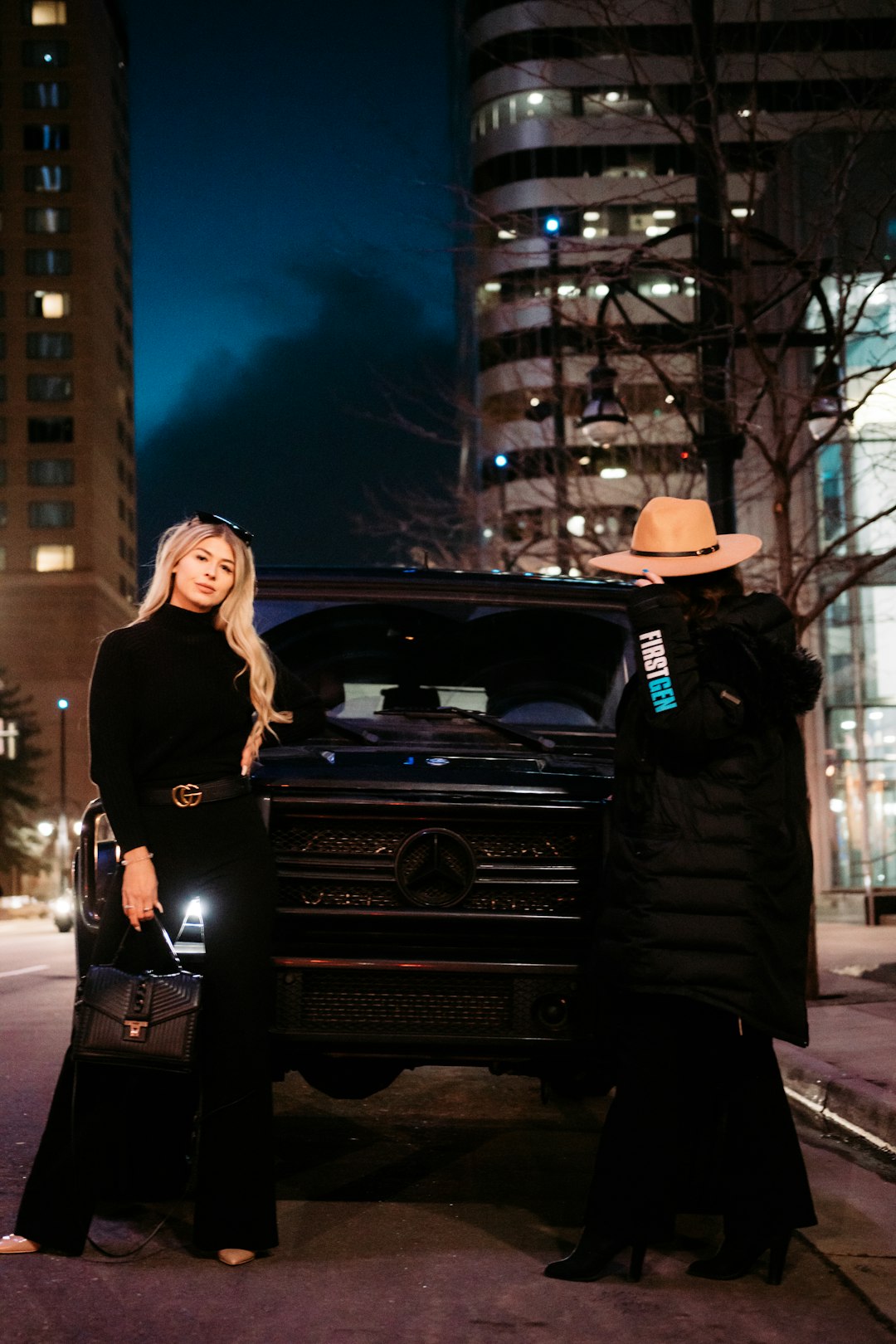 woman in black long sleeve dress standing beside black car during night time