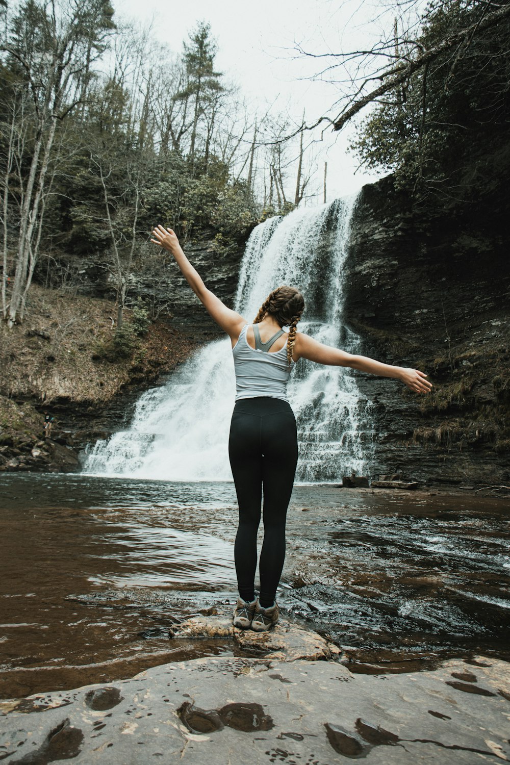 woman in white tank top and black leggings standing on water falls