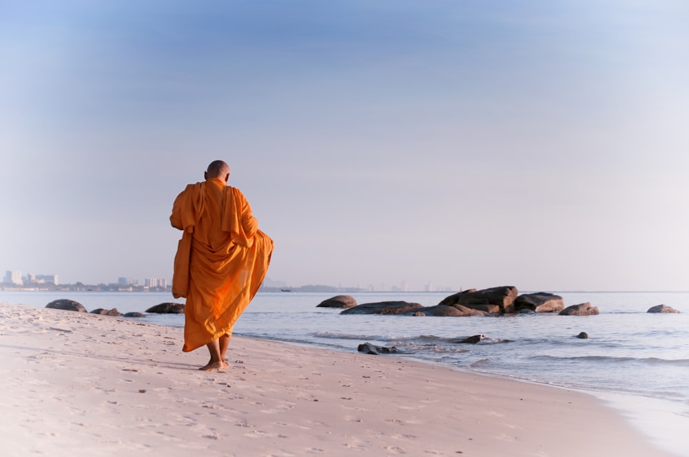 낮에 해변을 걷고 있는 주황색 가운을 입은 남자