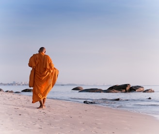 man in orange robe walking on beach during daytime