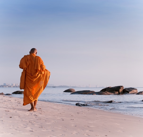 man in orange robe walking on beach during daytime