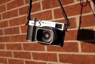 A vintage film camera with leather straps hanging against a rustic wall.