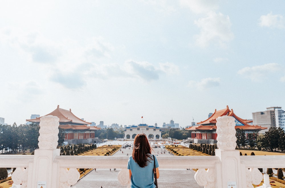 woman in blue long sleeve shirt standing on white concrete building during daytime