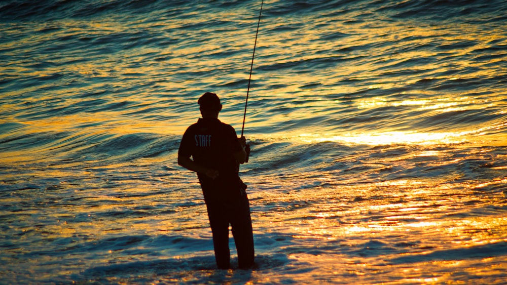 silhouette of man fishing on sea during sunset