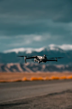 Aerial view of a tactical VTOL drone in flight over a rugged border landscape at dawn.