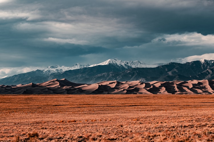 sand dunes in front of snow capped mountains