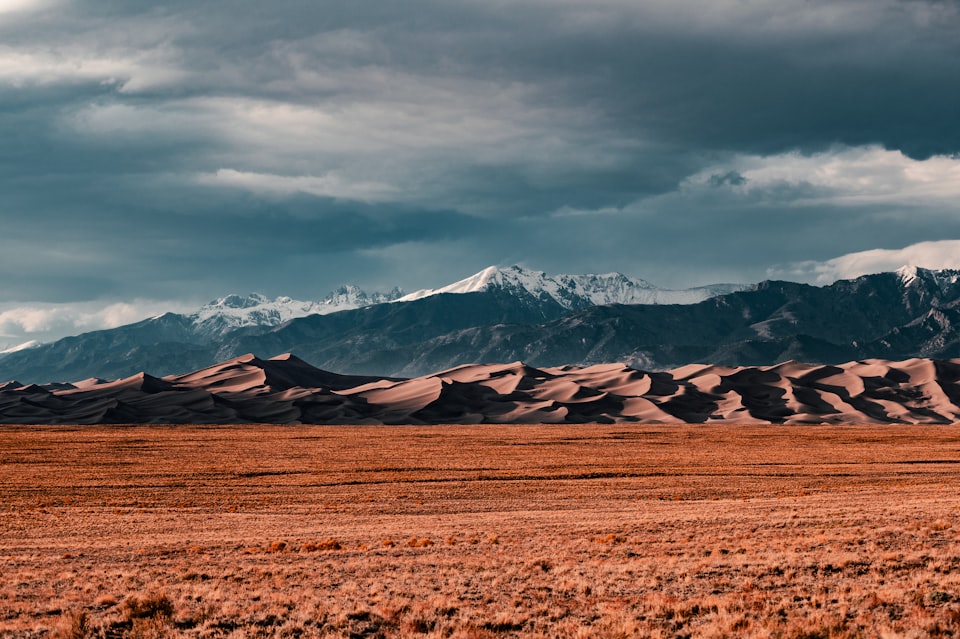 sand dunes in front of snow capped mountains