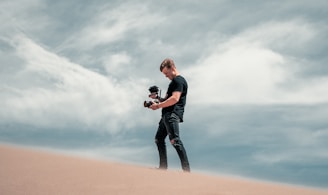 man in black jacket and black pants standing on brown sand during daytime