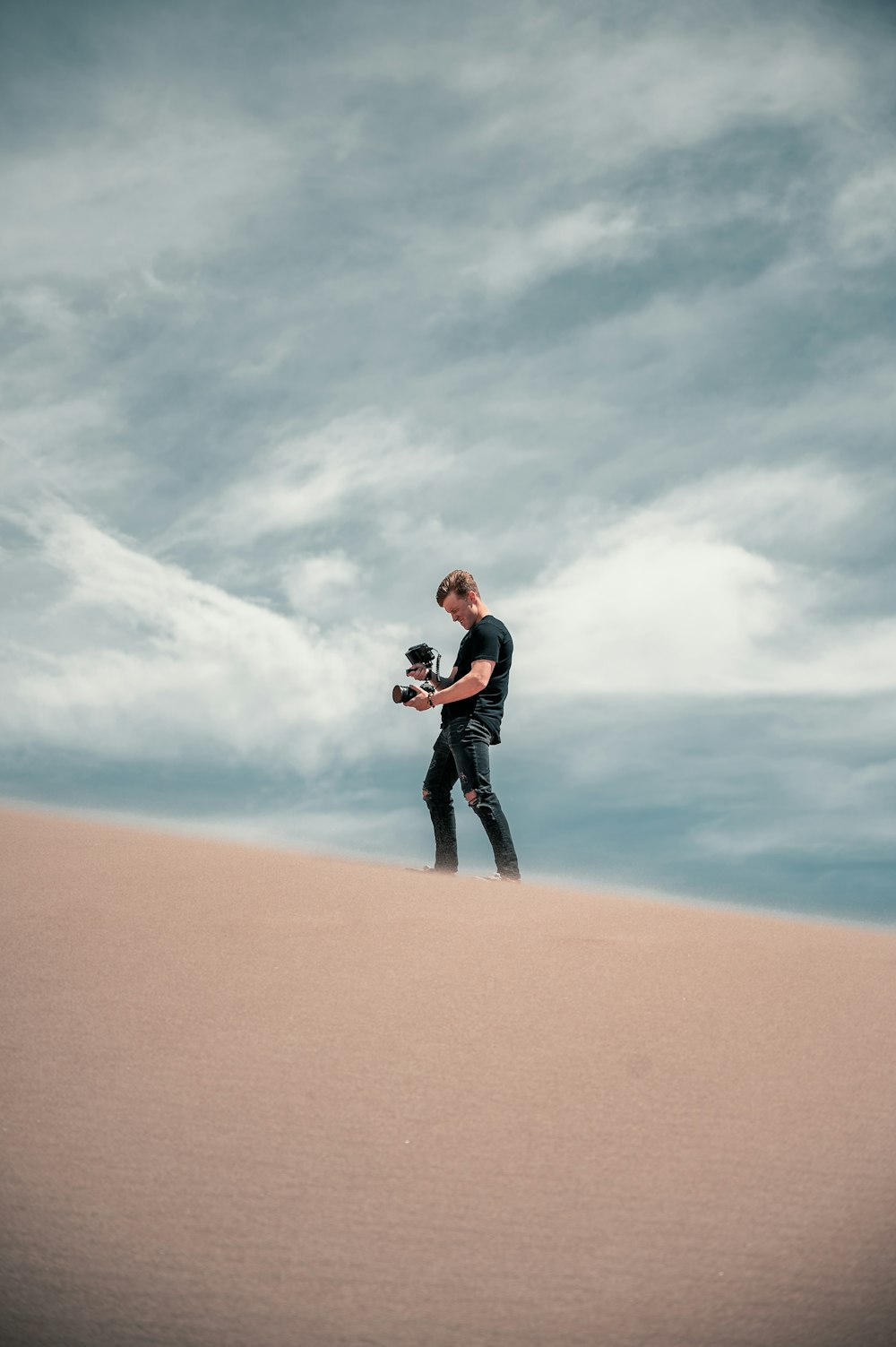 homme en veste noire et pantalon noir debout sur le sable brun pendant la journée