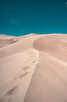 A hidden mountain trail winding through soft beige sand dunes under a clear blue sky.