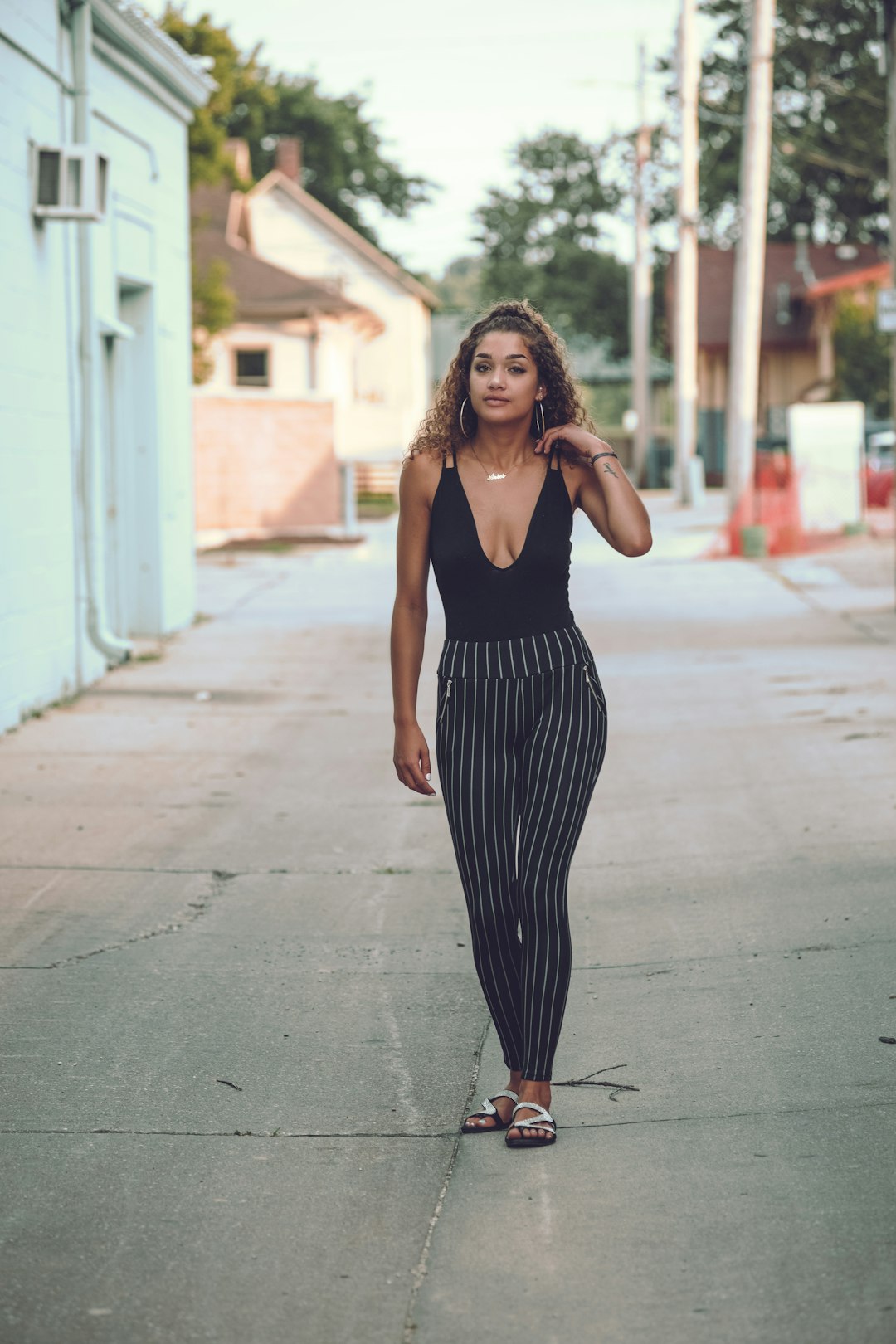 woman in black tank top and black and white striped pants standing on gray concrete pavement
