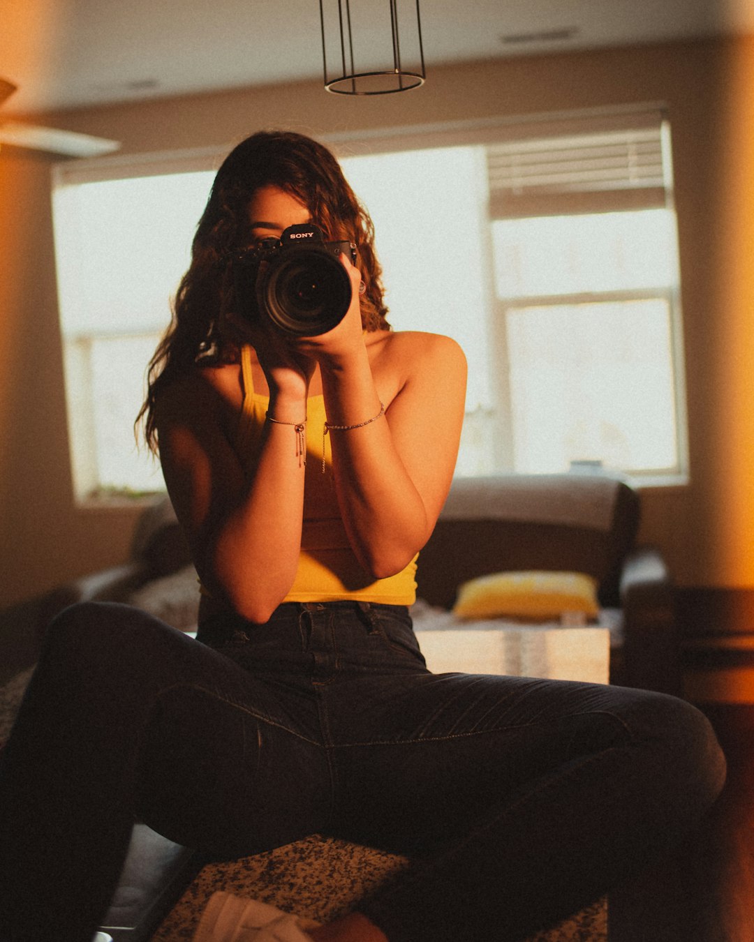 woman in yellow tank top and black denim jeans sitting on brown sofa