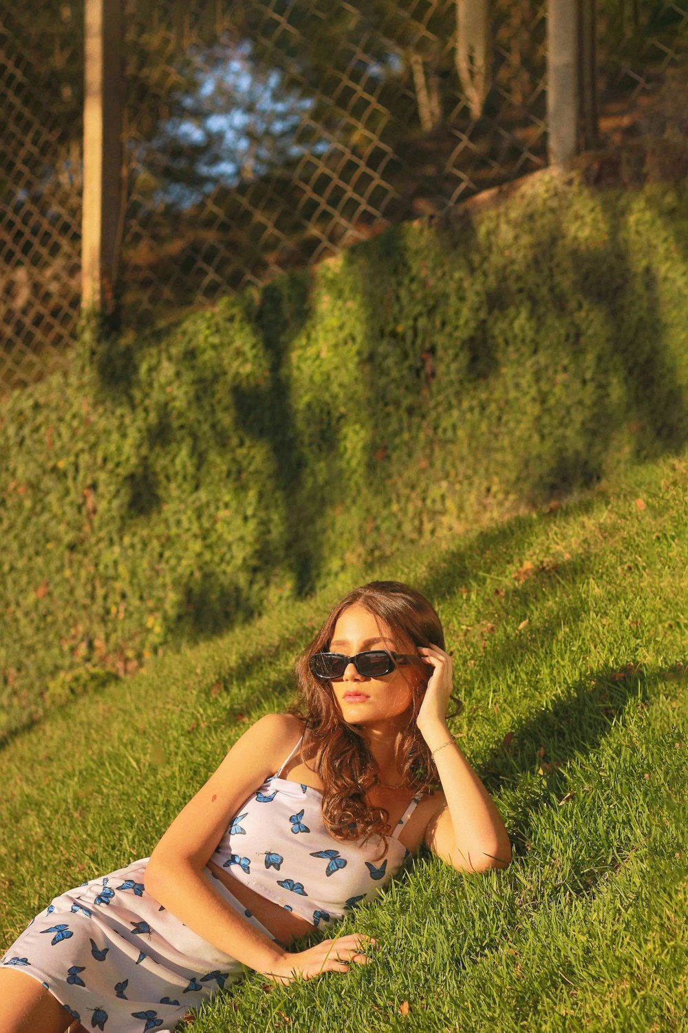 femme en débardeur floral blanc et noir couché sur le champ d’herbe verte pendant la journée