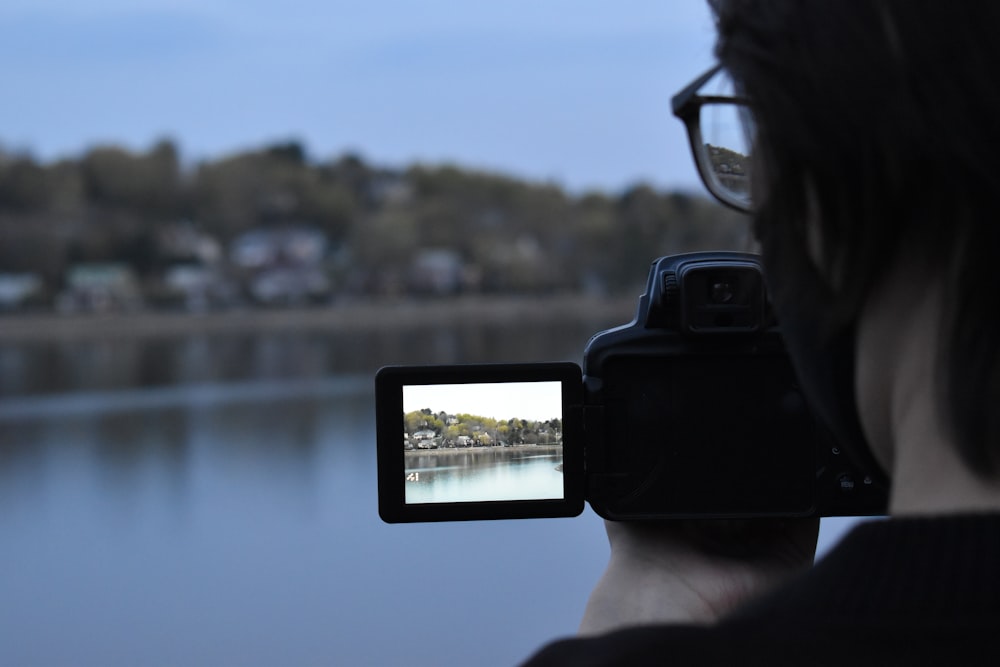 personne tenant un smartphone noir prenant des photos d’un plan d’eau pendant la journée