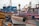 Multiple colorful fishing boats are docked at a waterfront with various names and numbers visible on their sides. Seagulls perch on some of the boats, and the dock is lined with weathered posts and ropes. The scene is calm and serene, with overcast skies in the background.