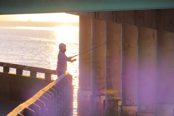 Close-up of a fisherman wearing a rugged hoodie while casting a line at dawn on a misty lake.