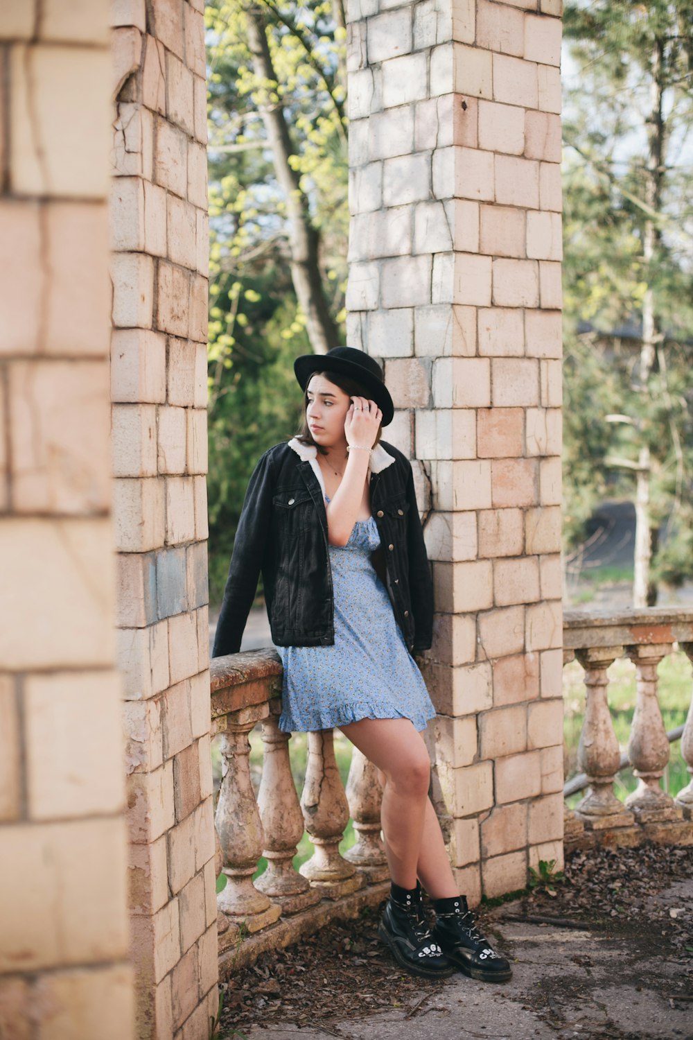 woman in black coat and blue denim skirt standing beside brown brick wall during daytime