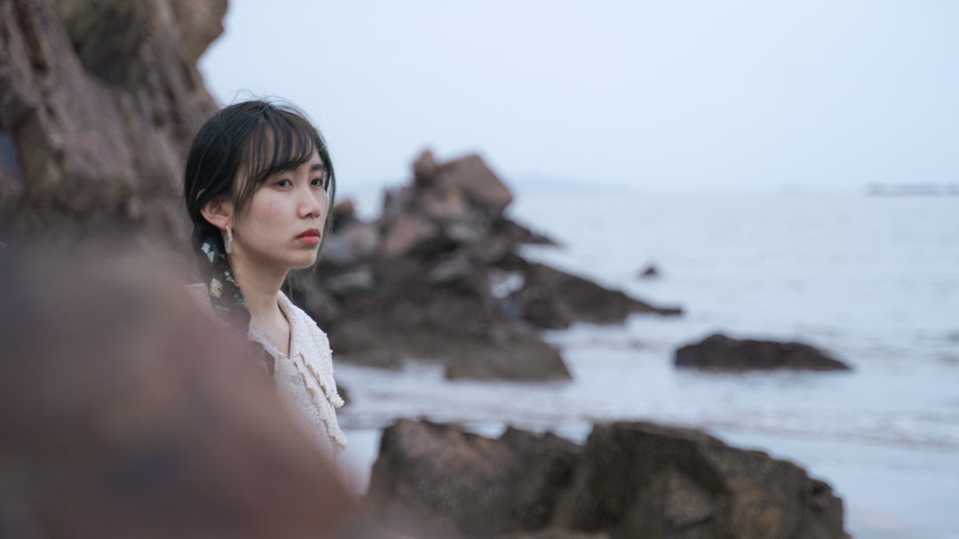 woman in white sleeveless top standing on rocky shore during daytime