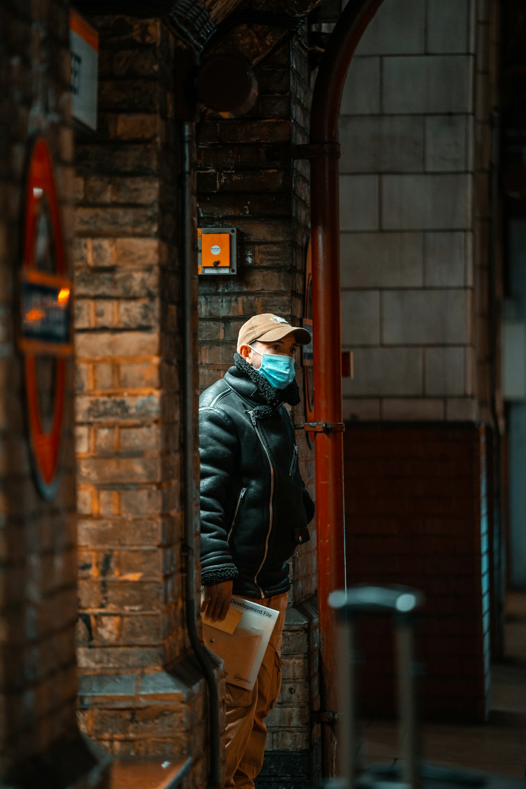 man in black leather jacket and brown knit cap standing beside brown wooden door