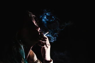 Close-up of a punk rock antihero with a scarred face and a cigarette glowing in the dark.