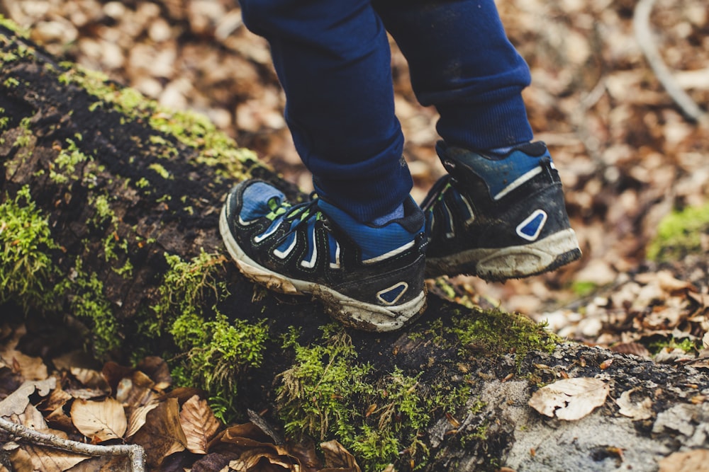 person in blue denim jeans and black and white nike sneakers standing on green moss