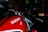A close-up of a red motorcycle tank with the brand name 'Ducati Monster' prominently displayed. The image focuses on the sleek design and shiny surface of the bike, highlighting the handlebar and part of the front suspension.