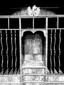 An intricately designed wooden structure featuring shelves and vertical slots with a decorative element on top. The central section includes multiple drawers with round knobs, showcasing a wood grain pattern.