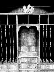 An intricately designed wooden structure featuring shelves and vertical slots with a decorative element on top. The central section includes multiple drawers with round knobs, showcasing a wood grain pattern.