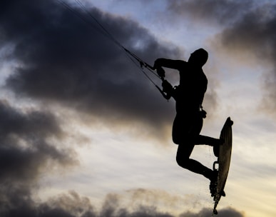 silhouette of man riding on skateboard under cloudy sky during daytime