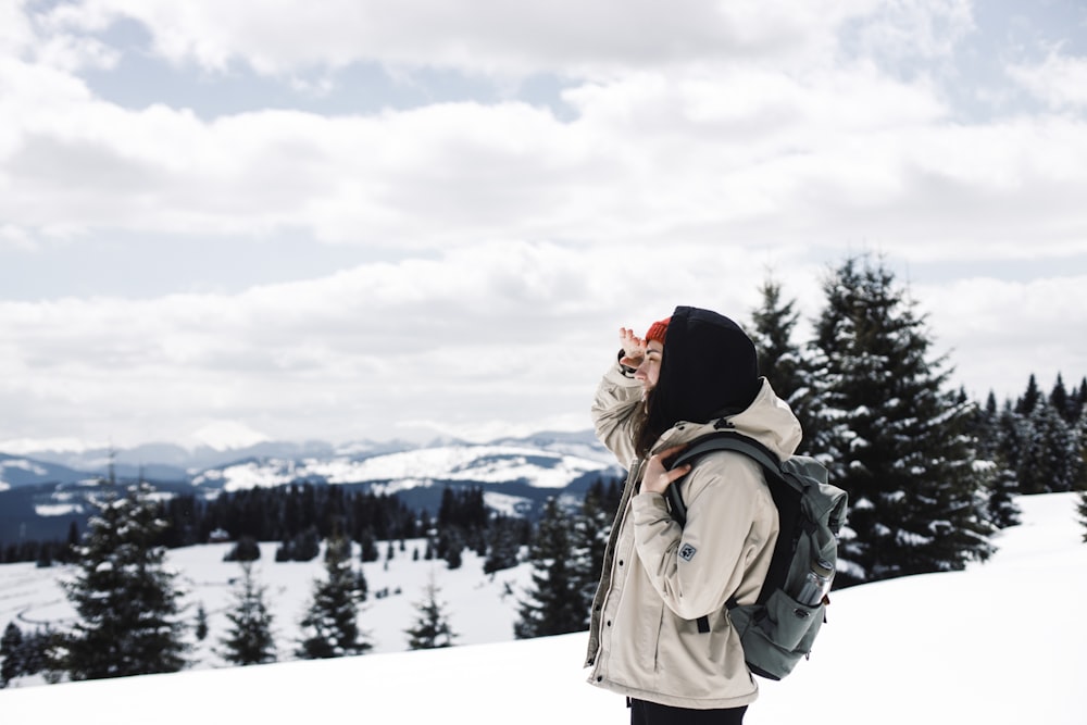 person in black knit cap and brown jacket standing on snow covered ground during daytime