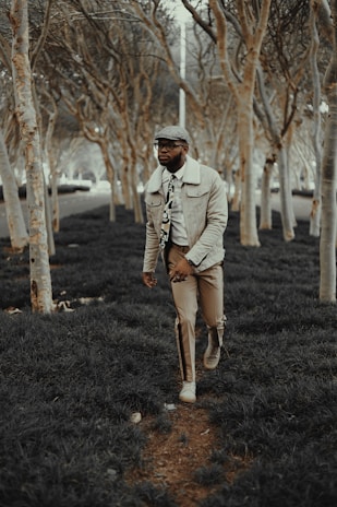 A man in a cozy knit sweater and tailored trousers walking through a park in autumn.
