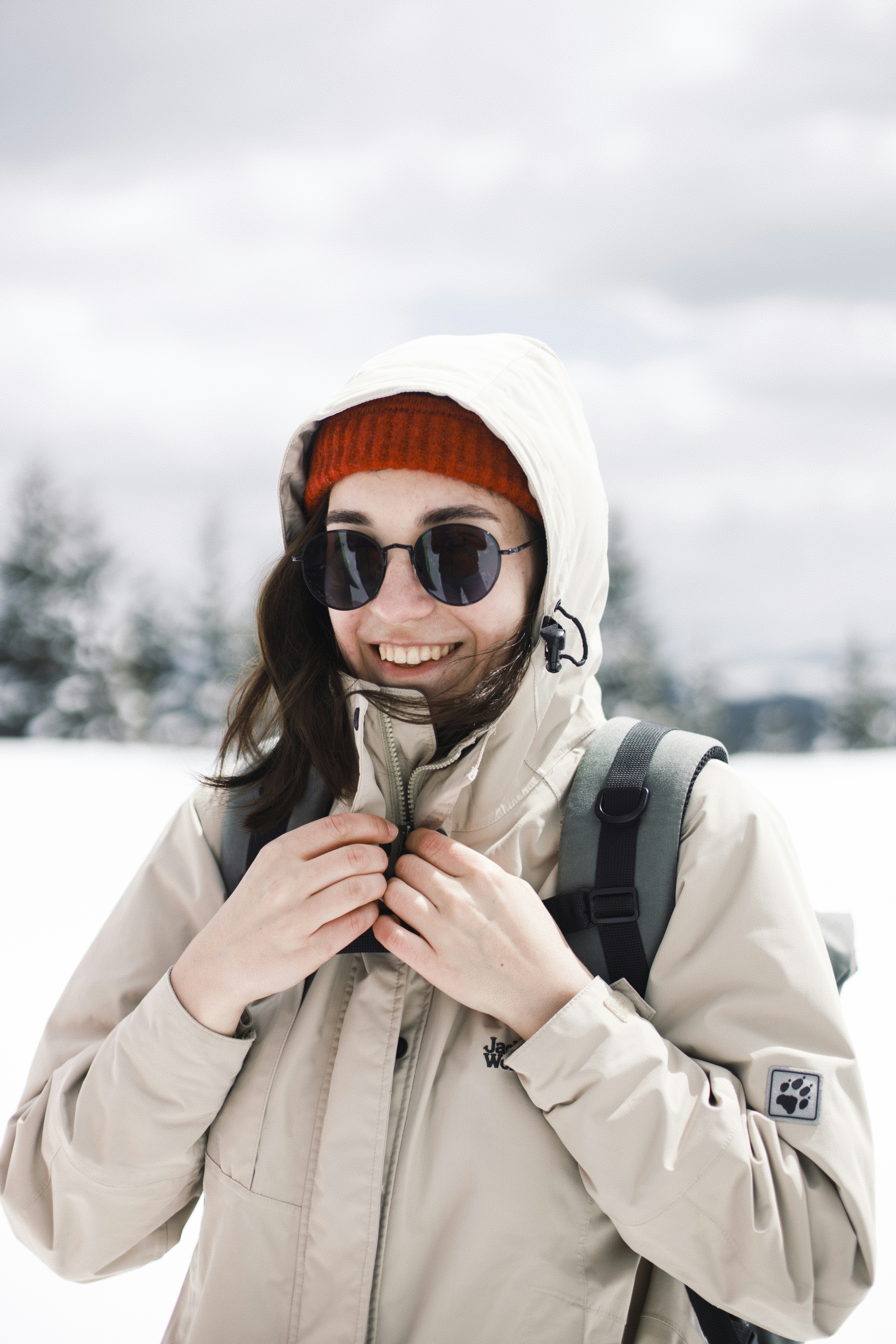 woman in white coat wearing orange sunglasses and white knit cap