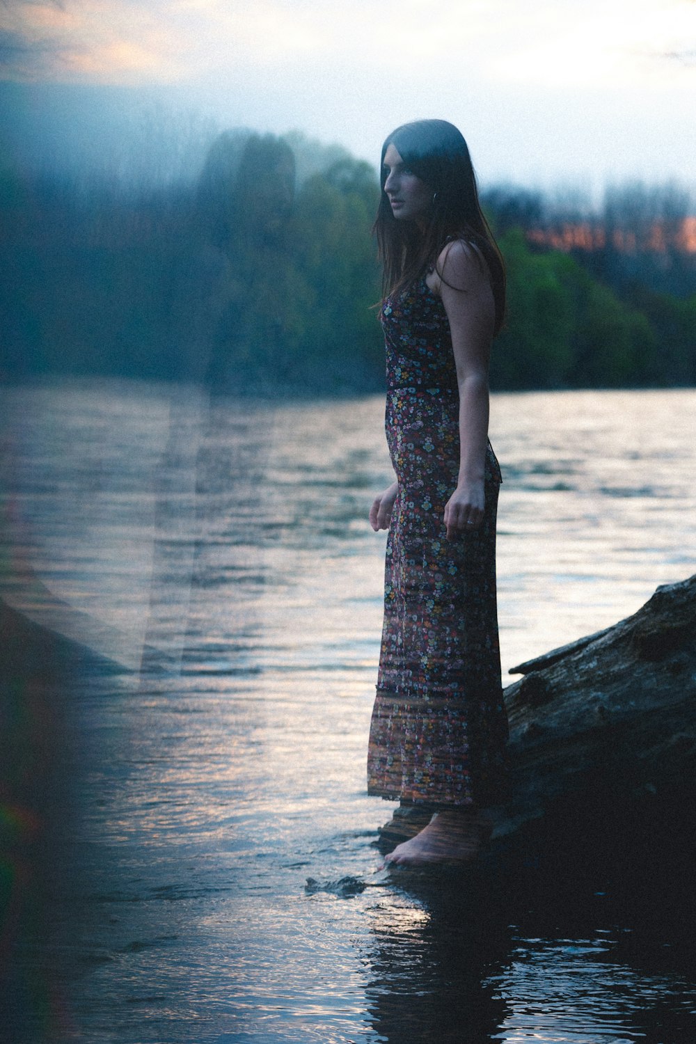 woman in black and white floral spaghetti strap dress standing on rock near body of water