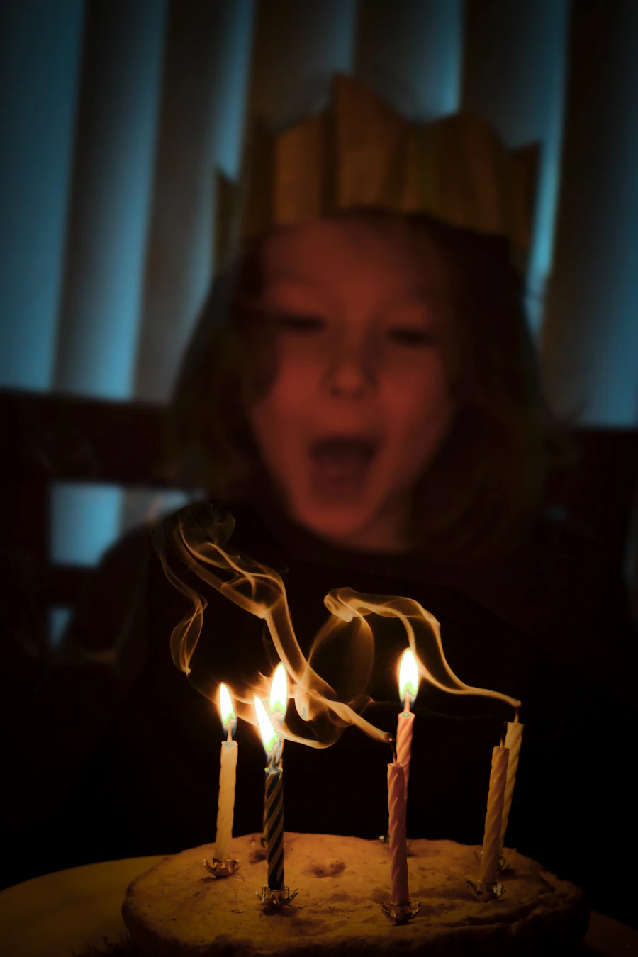 Child blowing out candles on a birthday cake surrounded by family