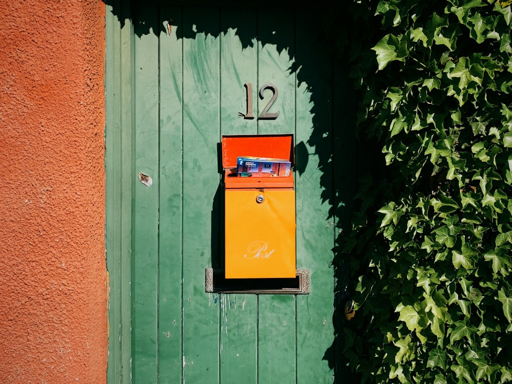 yellow and red mail box on green wooden door