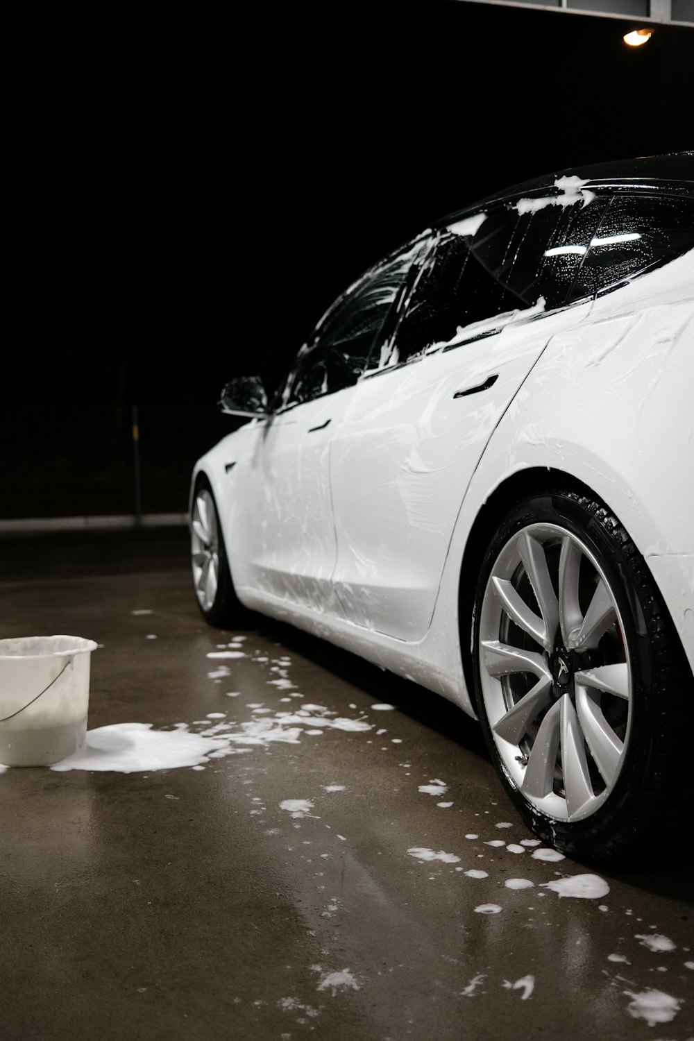Before: white Tesla covered in thick foam mid-wash at night