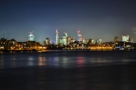 A night time cityscape featuring illuminated skyscrapers reflecting beautifully on the river.