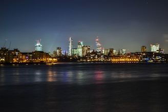 A night time cityscape featuring illuminated skyscrapers reflecting beautifully on the river.