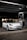 A sleek, white Tesla car, parked under a canopy at a gas station or charging point during nighttime. The car is positioned near a charging station, and the surroundings are dimly lit with a few lights visible in the background.