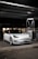 A sleek, white Tesla car, parked under a canopy at a gas station or charging point during nighttime. The car is positioned near a charging station, and the surroundings are dimly lit with a few lights visible in the background.