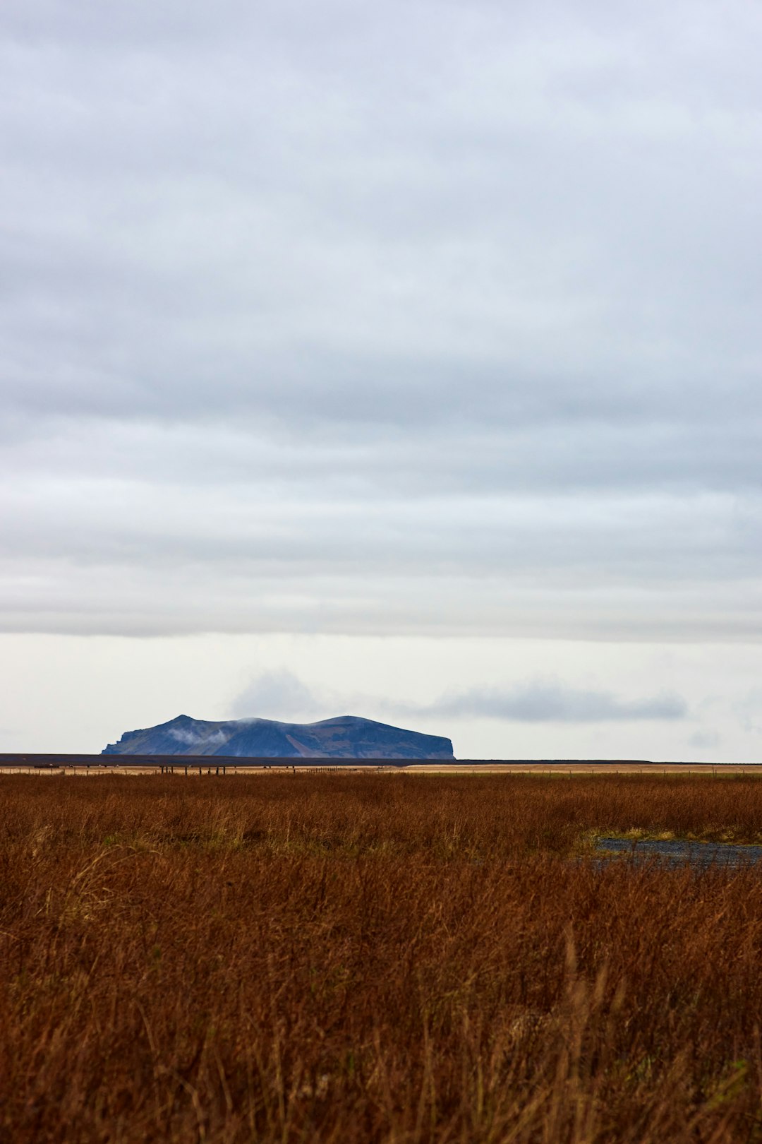 brown grass field near mountain under white clouds during daytime