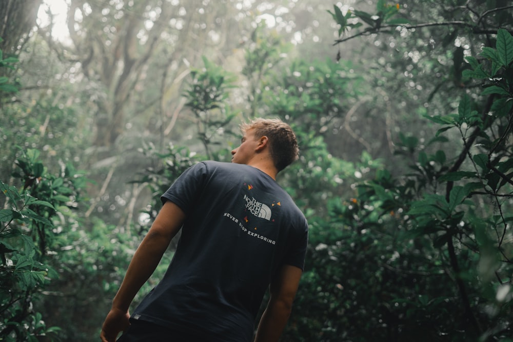 man in black crew neck t-shirt standing near green trees during daytime