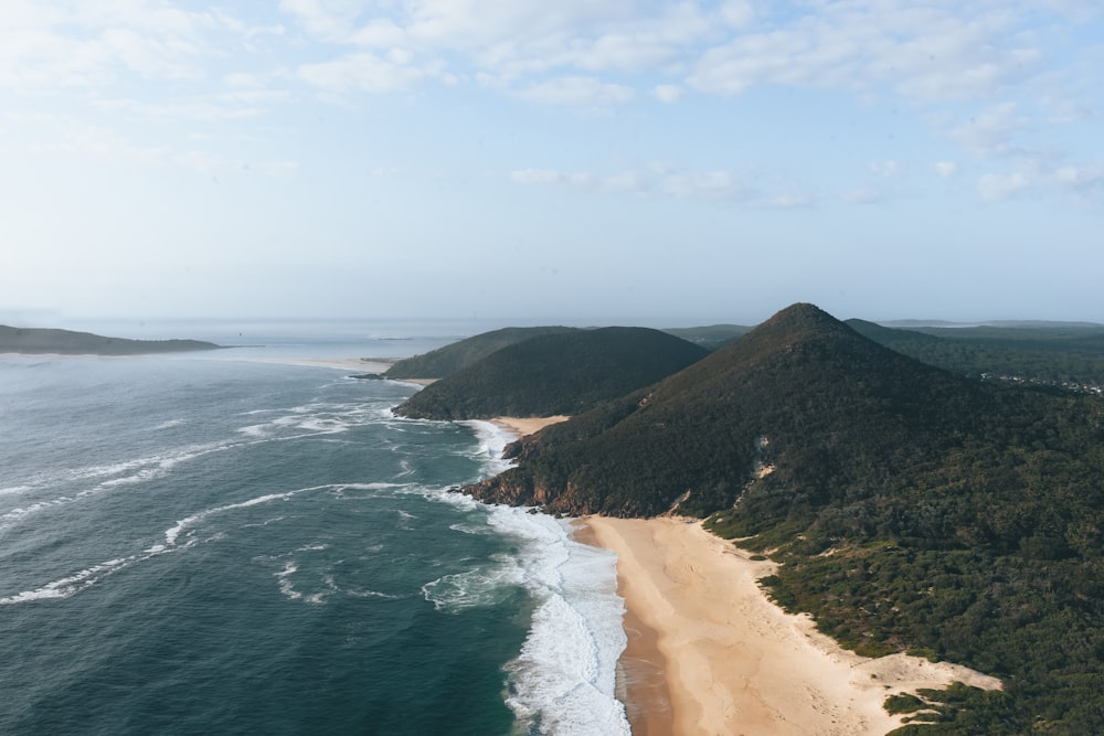 brown sand beach near green mountain under blue sky during daytime