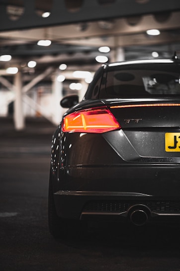 A sleek black car with a glossy vinyl wrap and tinted windows under soft studio lighting against a dark background.
